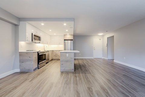 an empty living room with a kitchen with stainless steel appliances